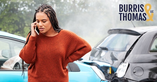 woman on the phone standing next to a car accident